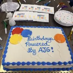 A sheet cake reading &ldquo;Birthdays Powered By AJG!&rdquo;