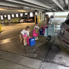 Two young children and an adult carrying gift bags in a parking garage